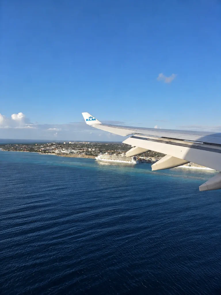 View past a KLM aircraft wing towards Oranjestad and cruise ships off Aruba